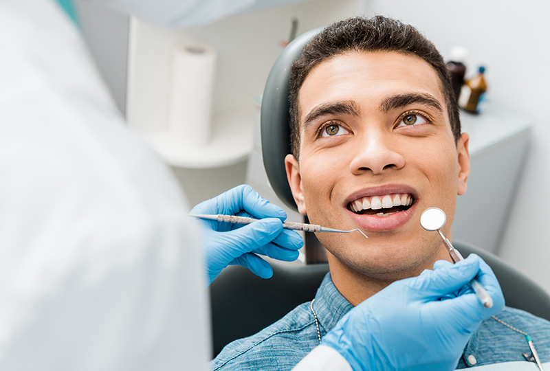 The image shows a dental patient with a broad smile, seated in a dental chair, receiving dental treatment from a dentist who is adjusting their braces.